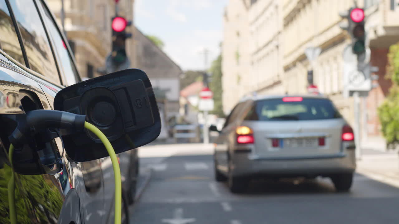 Electric car parked on the city street, with plugged charger, handheld shot