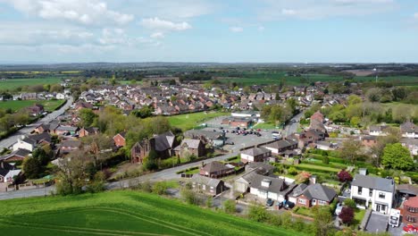 Aerial-view-rural-British-countryside-village-surrounded-by-idyllic-farmland-fields,-Cheshire,-England