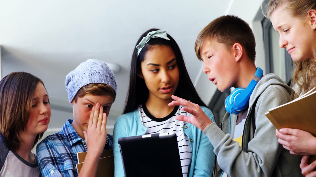 Group of school friends using digital tablet in corridor