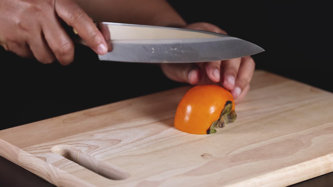 las manos cortando hábilmente un caqui maduro