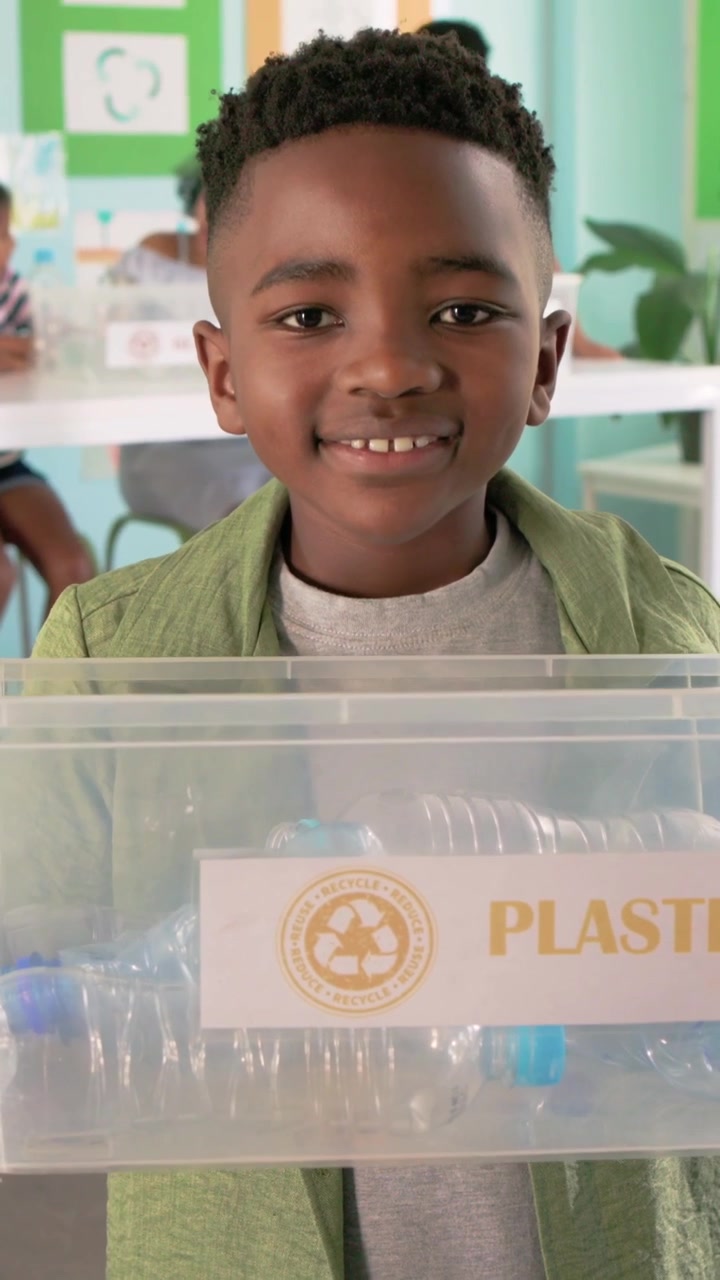 Video verticale: Studente che si muove e presenta un contenitore di PLASTICA con bottiglie in classe per il riciclo.