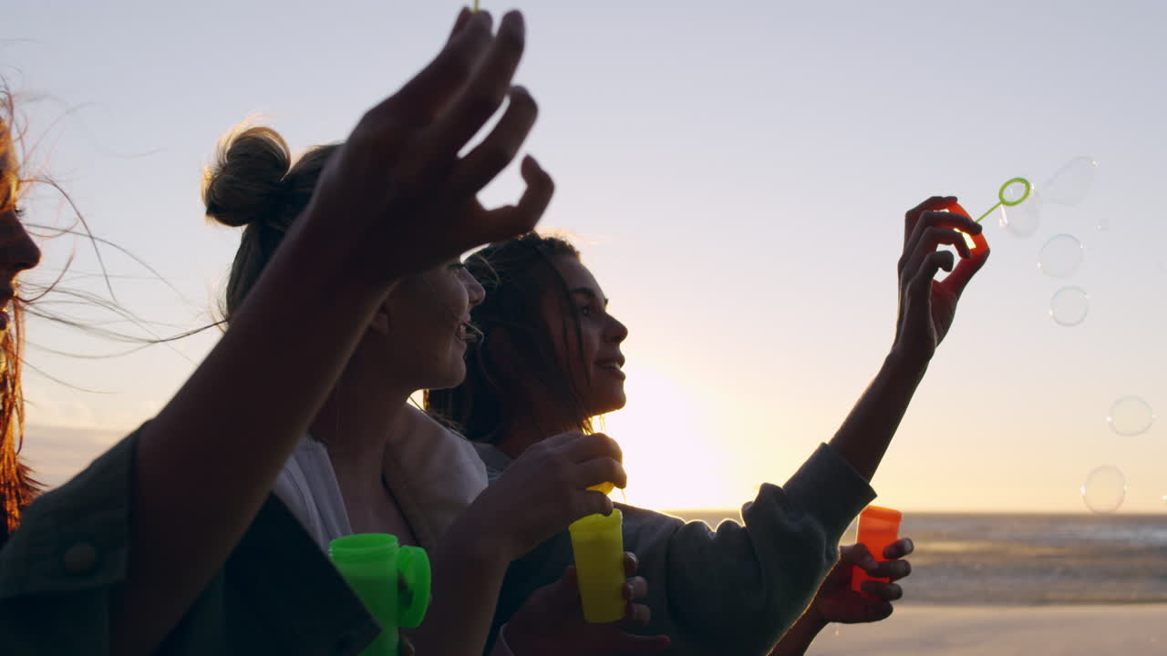 amigas soplando burbujas en la playa al atardecer en cámara lenta