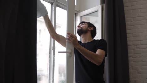 el hombre está limpiando la ventana, limpiando la superficie, usa un trapo, de pie en un apartamento moderno