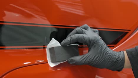 mano con guante negro aplicando recubrimiento cerámico en el exterior del coche utilizando bloque de espuma