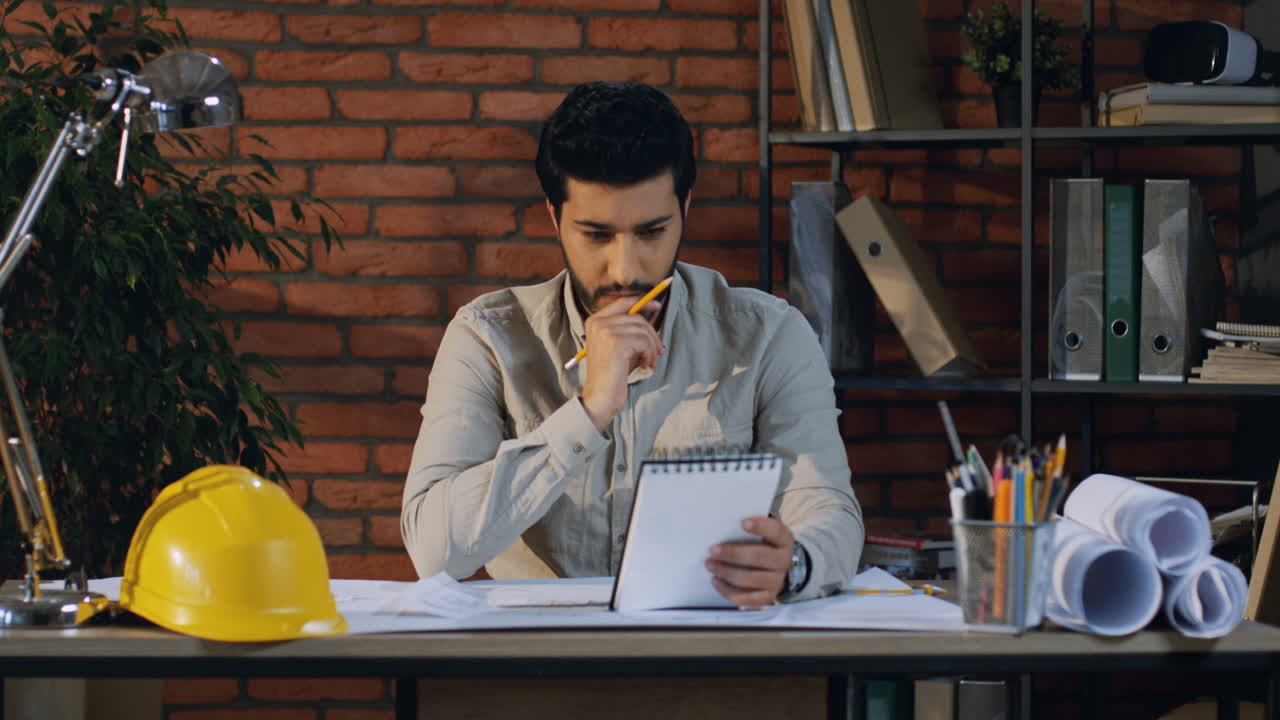joven arquitecto árabe sentado en la mesa de la oficina y pensando en las nuevas ideas y dibujos del proyecto
