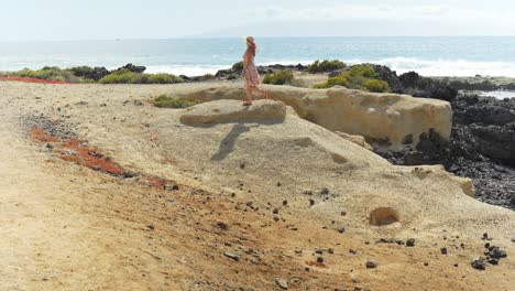 Frau-Im-Geblümten-Kleid-Läuft-über-Die-Felsbrocken-In-Strandnähe,-Statische-Zeitlupe