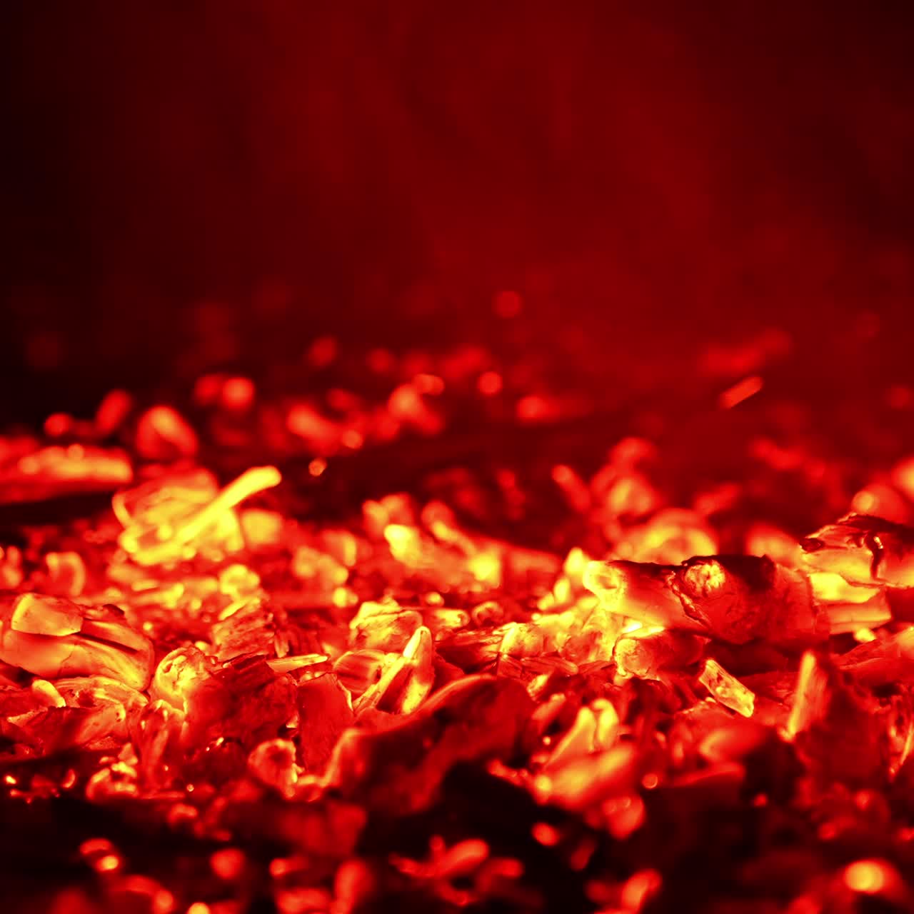 Glowing pieces of charcoal sparkling beautifully. Little flames of fire break out again. Close up