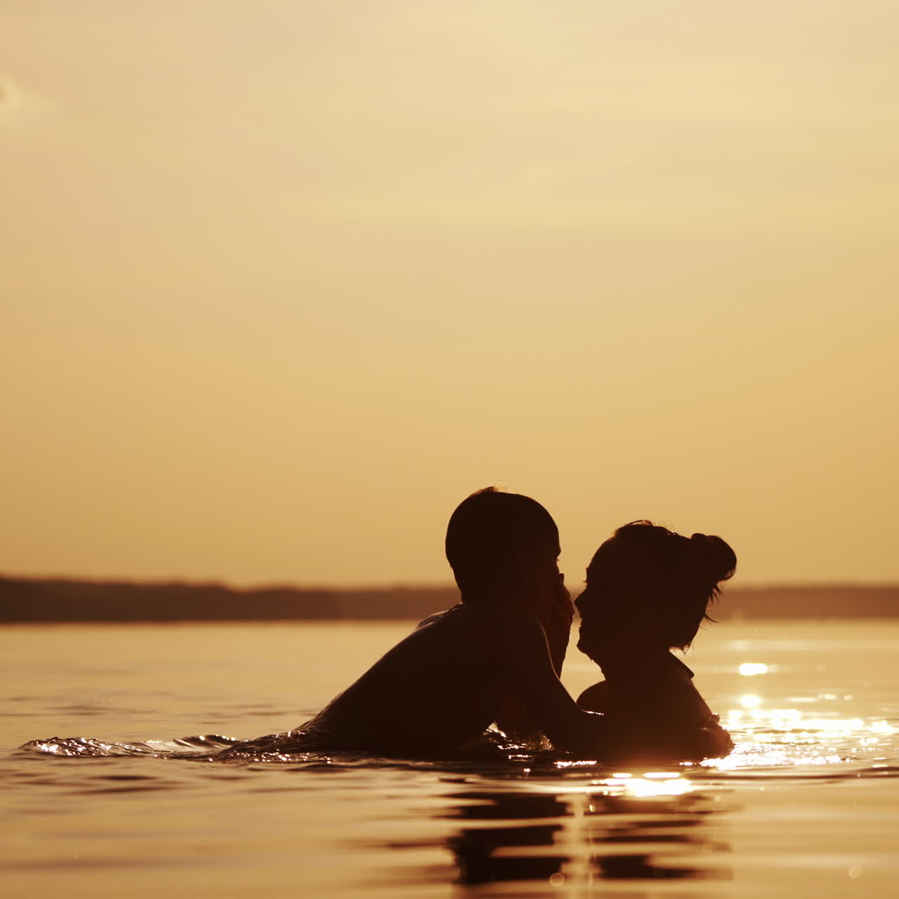 Mother having happy time together with her son in water. Joyful boy swimming in the river and a woman lifts him up in the evening in summer.