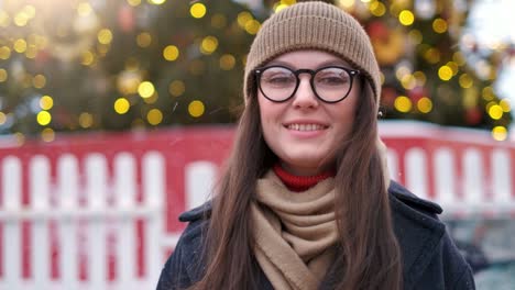 pretty woman stands on the city square among christmas decorations and looks straight into the camera