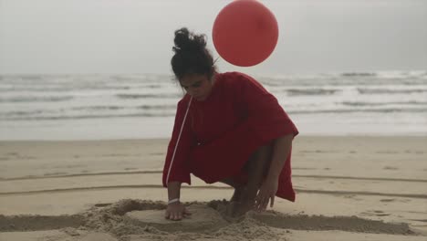 Slow-motion-shot-of-beautiful-woman-with-a-balloon-digging-in-the-sand-on-a-beach-to-create-a-design