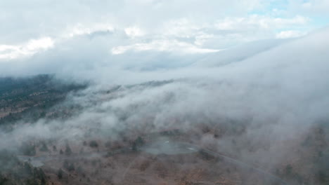 a misty landscape with clouds rolling over hills at dawn, aerial view