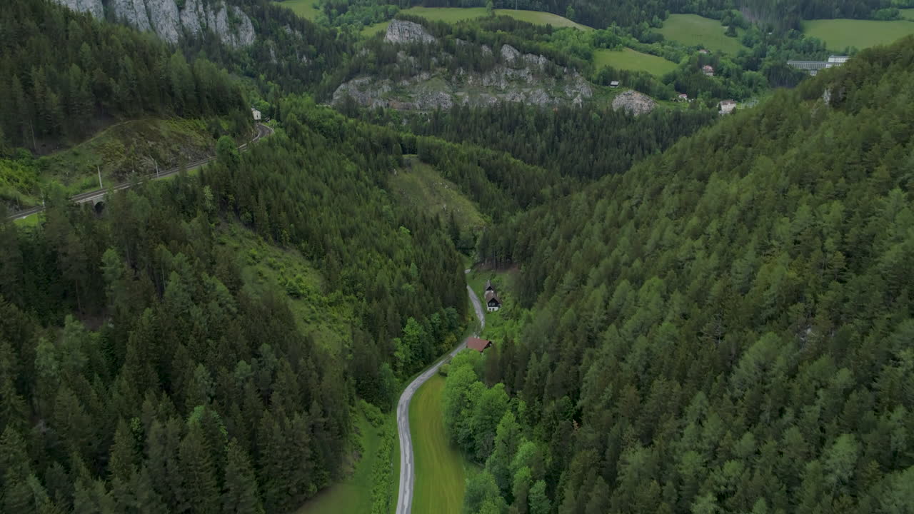 toma aérea de una calle en medio de un bosque junto a montañas y rieles, 4k uhd, semmering, austria