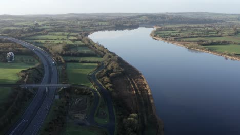 Peaceful-aerial-of-highway-traffic-next-to-wide-tranquil-rural-river