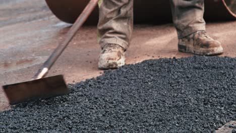 construction worker is scraping the excess asphalt layer off the patched street