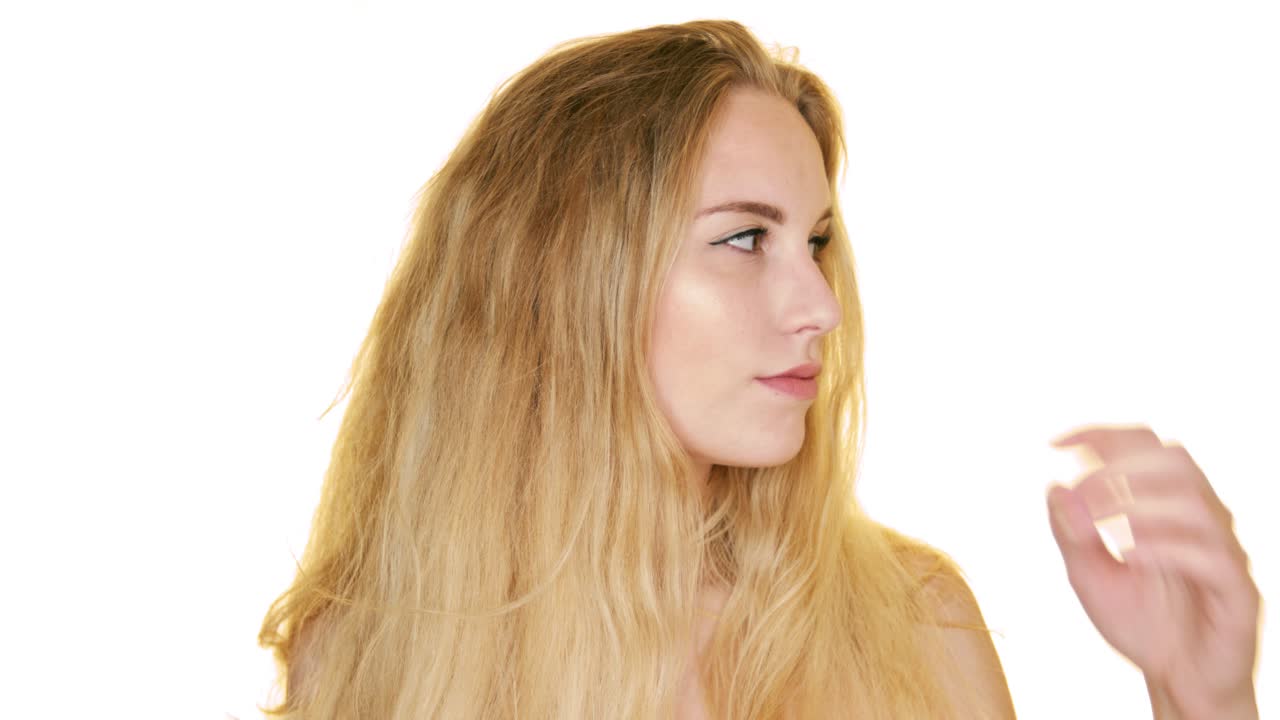 예쁜 금발 소녀는 흰색 배경에 포즈를 취하고 손으로 얼굴을 만지며 좌우로 보입니다.