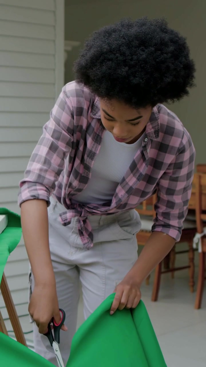 Vertical video: Coming with scissors, woman in pink top trimming fabric to cover frame on porch