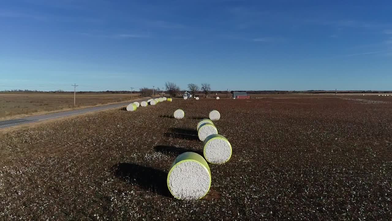 toma aérea de drones de barrido de una granja de algodón del medio oeste con pacas frescas de algodón cosechado envuelto en material amarillo brillante contra un cielo azul abierto