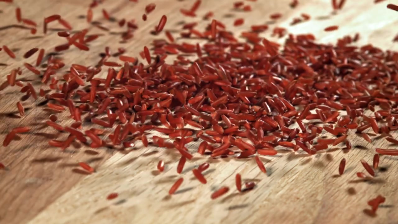 Grains de riz rouge tombant sur une surface en bois au ralenti.