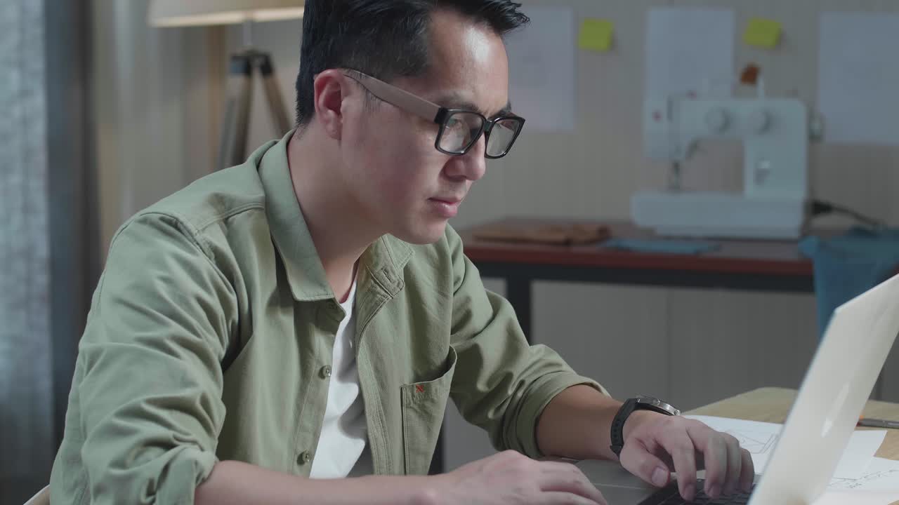 사무실에서 노트북을 사용하여 레이아웃 본드를 가진 아시아 남자 가방 디자이너의 클로즈업
