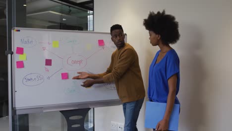 hombre de negocios afroamericano de pie en la pizarra dando una presentación a un colega