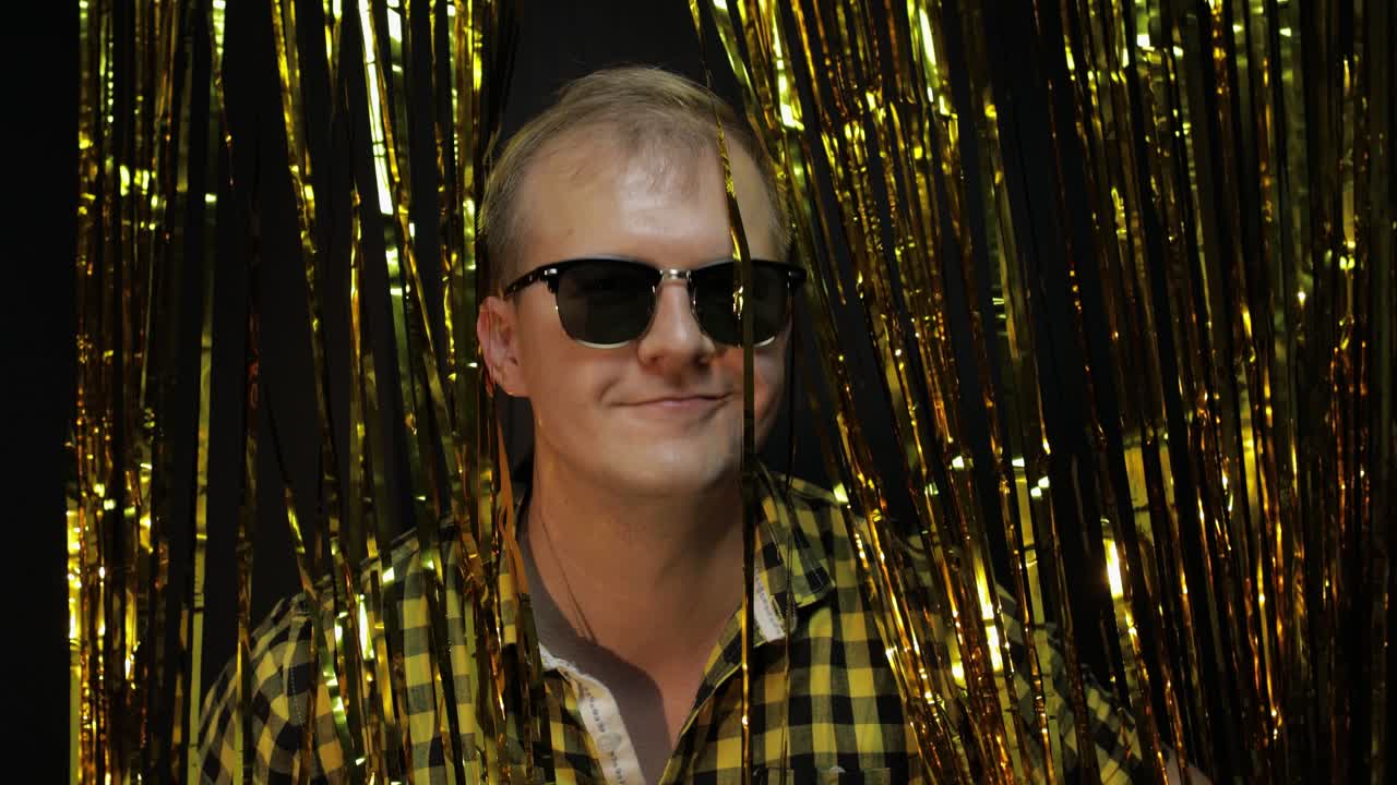 Valkoihoisen miehen muotokuva poseeraamassa mustaa taustaa vasten. Kultaiset kiiltävät foliosuikaleet. Juhlat, musiikki, disko.