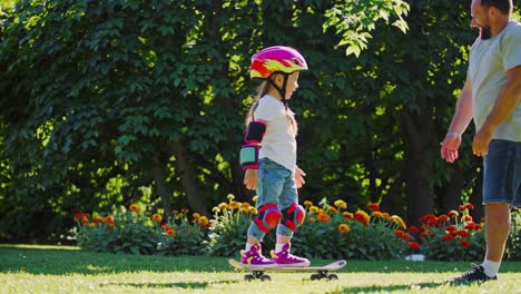 father teaching daughter to skateboard in park