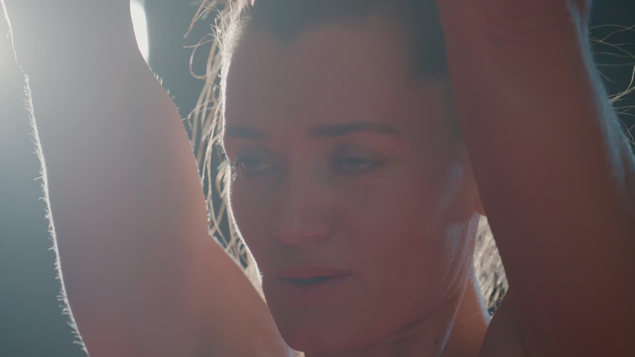 Close-up of Determined Woman Lifting Dumbbell in Gym with Backlight