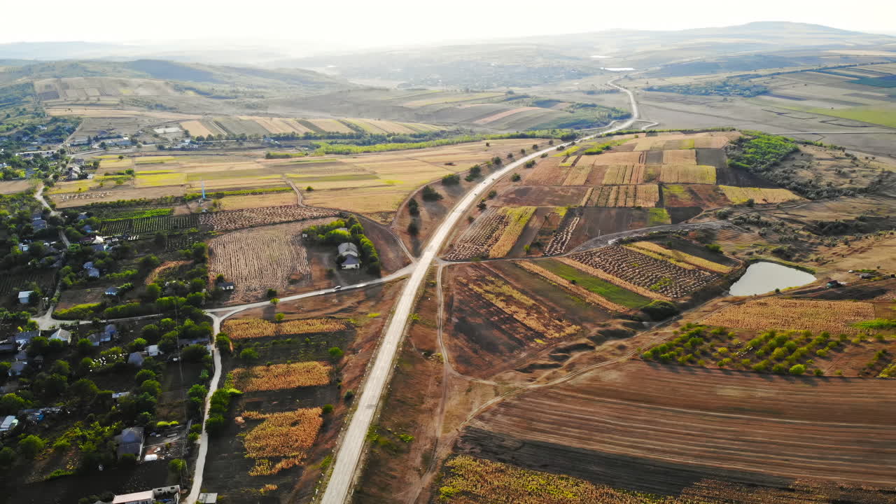 Aerial drone view of a road with moving cars in highland. Small village and green hills at sunset. Balti, Moldova