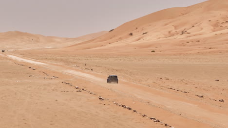 a 4x4 vehicle driving through the barren desert landscape of the empty quarters, oman