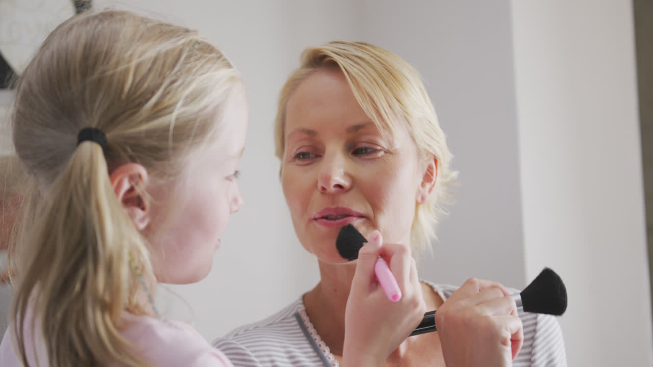 vista lateral de una mujer caucásica y su hija aplicando maquillaje