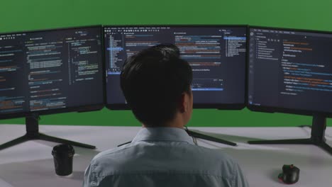 back view of asian man developer thinking about something then raising his index finger while write code with multiple computer screens in green screen studio