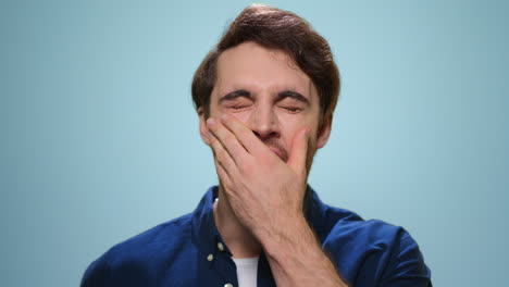 closeup lazy man yawning in studio. tired guy posing on blue background