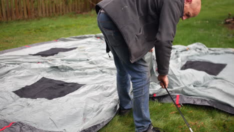 mature bald man threading tent poles through a tent at a campsite