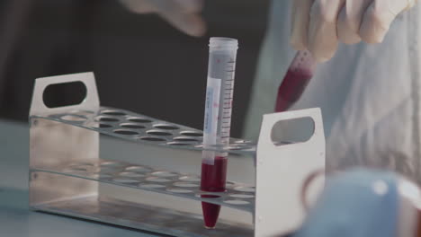 test tube with blood sample in holder and hand in rubber glove picking it up, laboratory detail