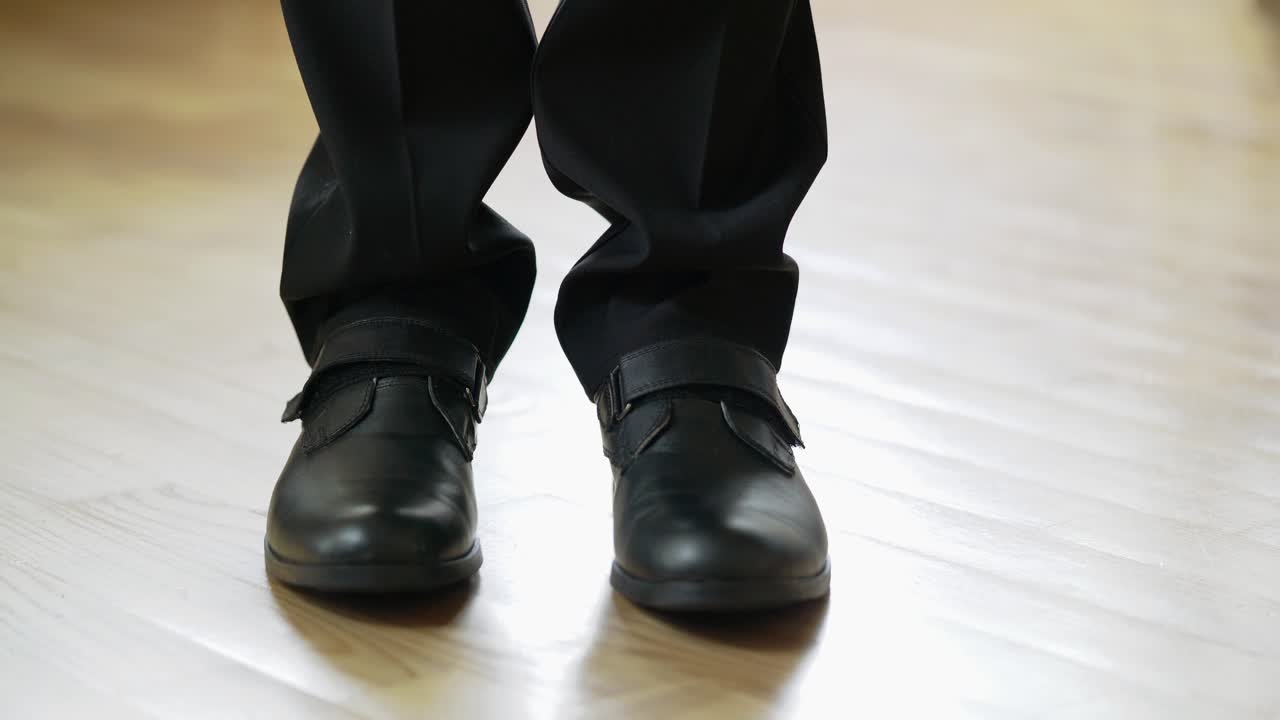 Male's legs wearing elegant shoes come into the room, stand for a while and go away. A pair of stylish shoes on a man in black suit on the floor inside