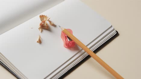 Close-up-of-open-notebook-with-pencil-and-pencil-sharpener-on-beige-background,-in-slow-motion