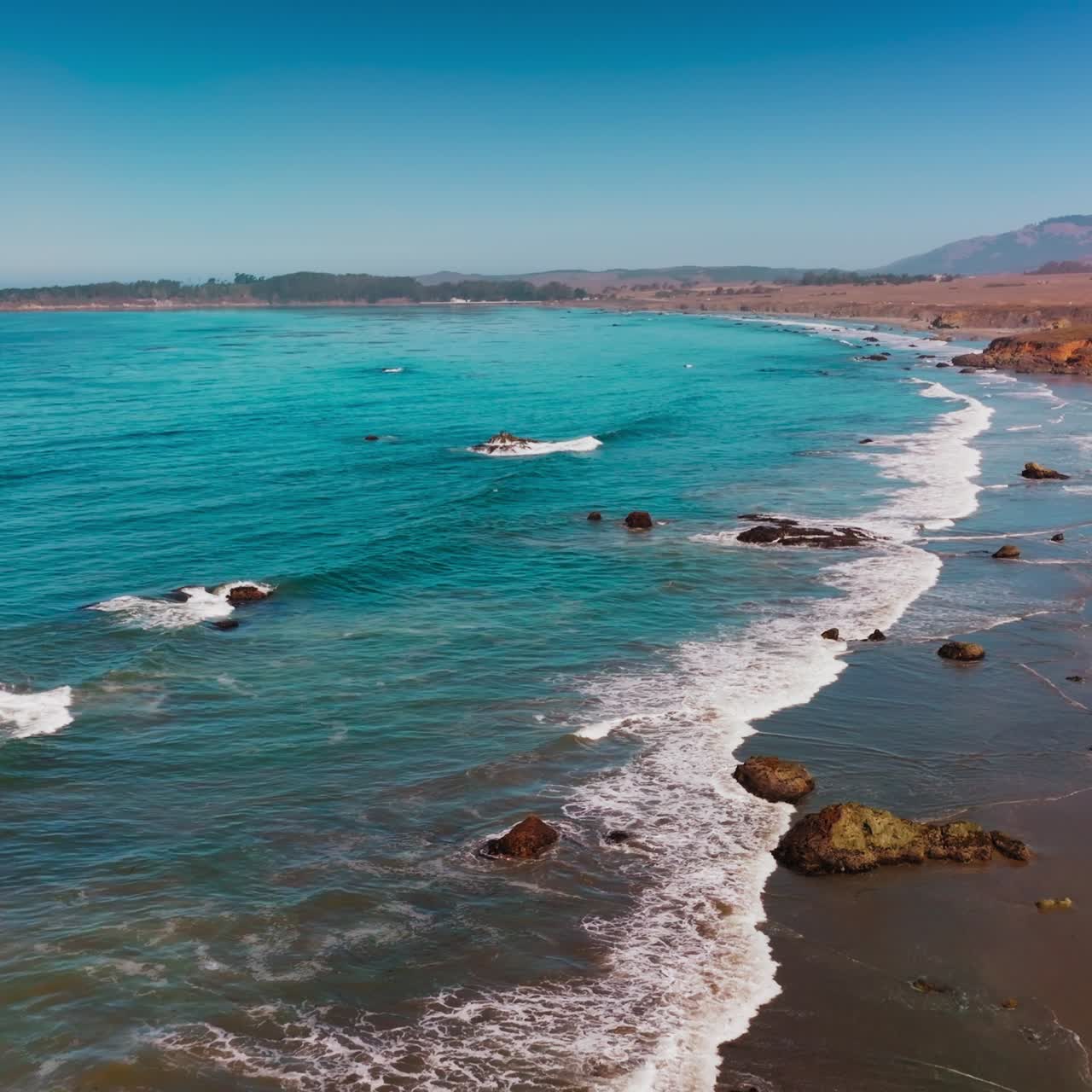 Peaceful mesmerizing view of little waves slowly moving to the sandy shore on sunny day. Scenery of Morro Bay, California, USA from top