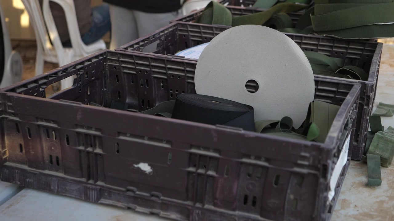 Close-up of a plastic crate containing a large spool and fabric materials, set in an industrial workspace