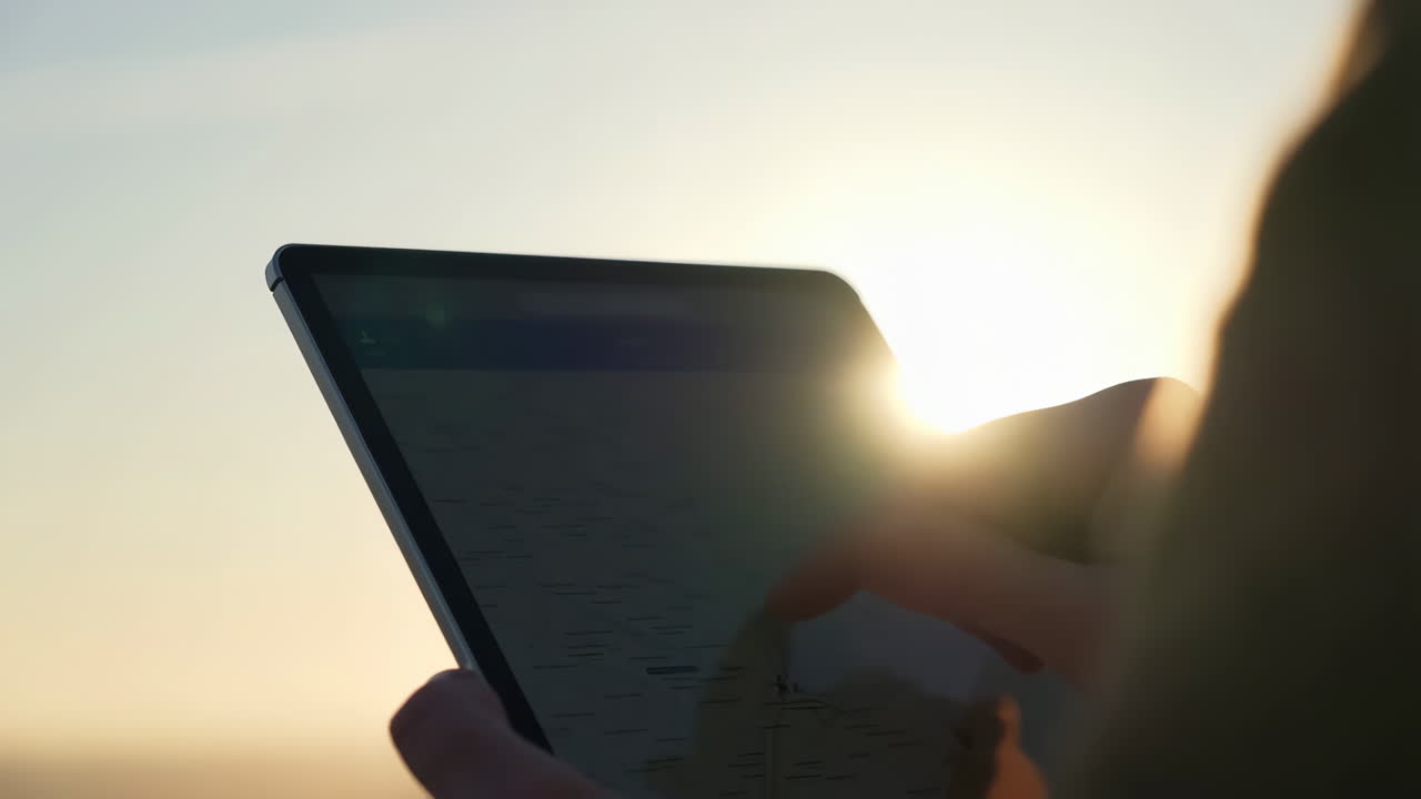 Person Using a Tablet Against a Bright Sunset or Sunrise