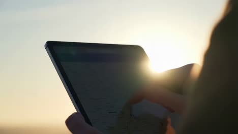 person using a tablet against a bright sunset or sunrise