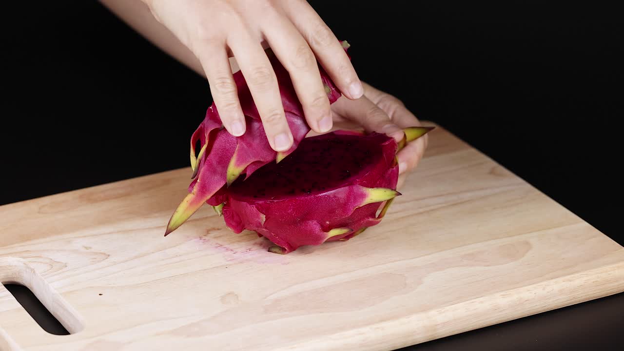 Hands cutting and displaying dragon fruit halves