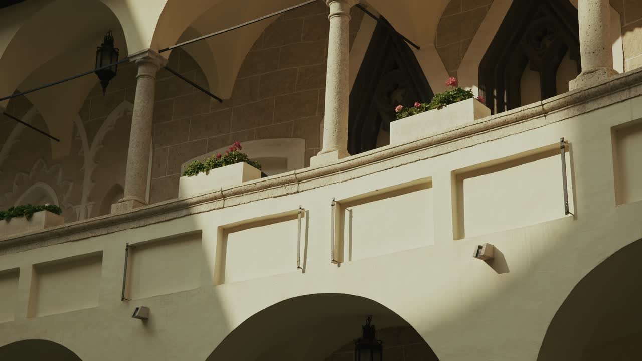 Soft sunlight casts shadows on an elegant arched balcony with flowers and stone columns
