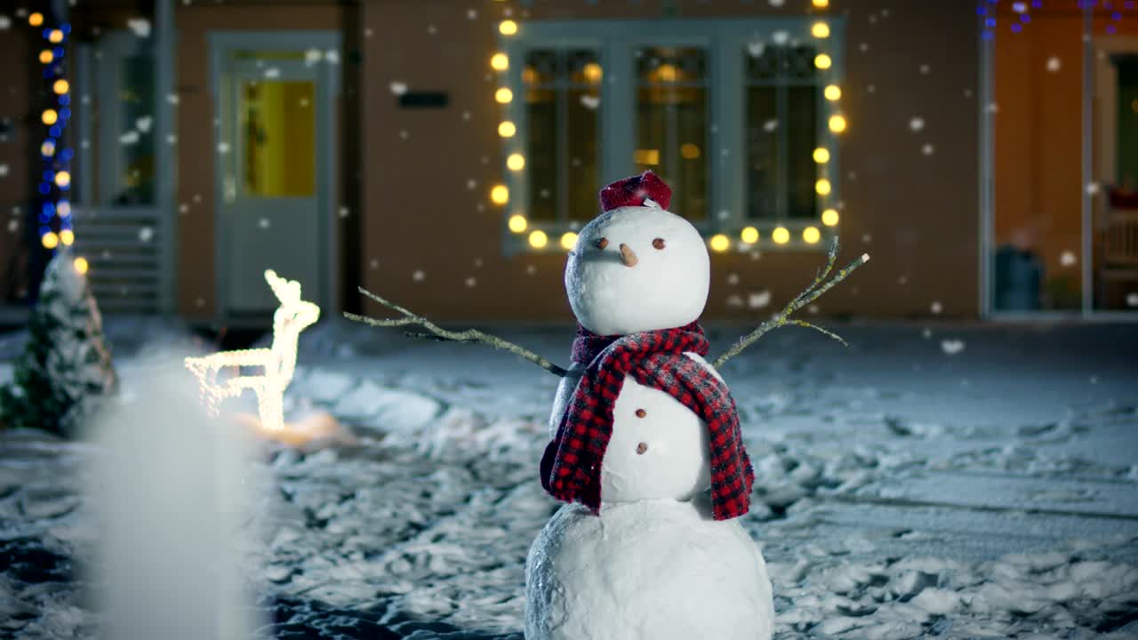 Funny Snowman Wearing Hat and Scarf Standing in the Backyard of the Idyllic House Decorated with Garlands on Christmas Eve. Soft Snow is Falling on that Magical Winter Evening.