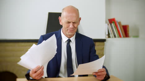 een depressieve zakenman zit aan een bureau naar papierwerk te kijken