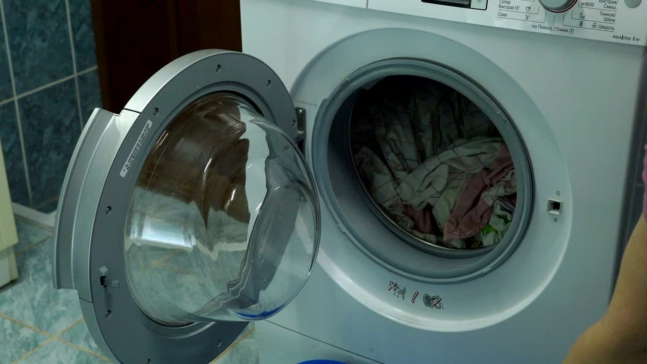 Woman opens the lid of the washing machine. She takes a clean wet laundry from the washing machine. Woman closes the lid of the washing machine.