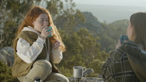 dos jóvenes excursionistas bebiendo té caliente del termo mientras se sientan en el acantilado de la montaña en un soleado día de otoño 1