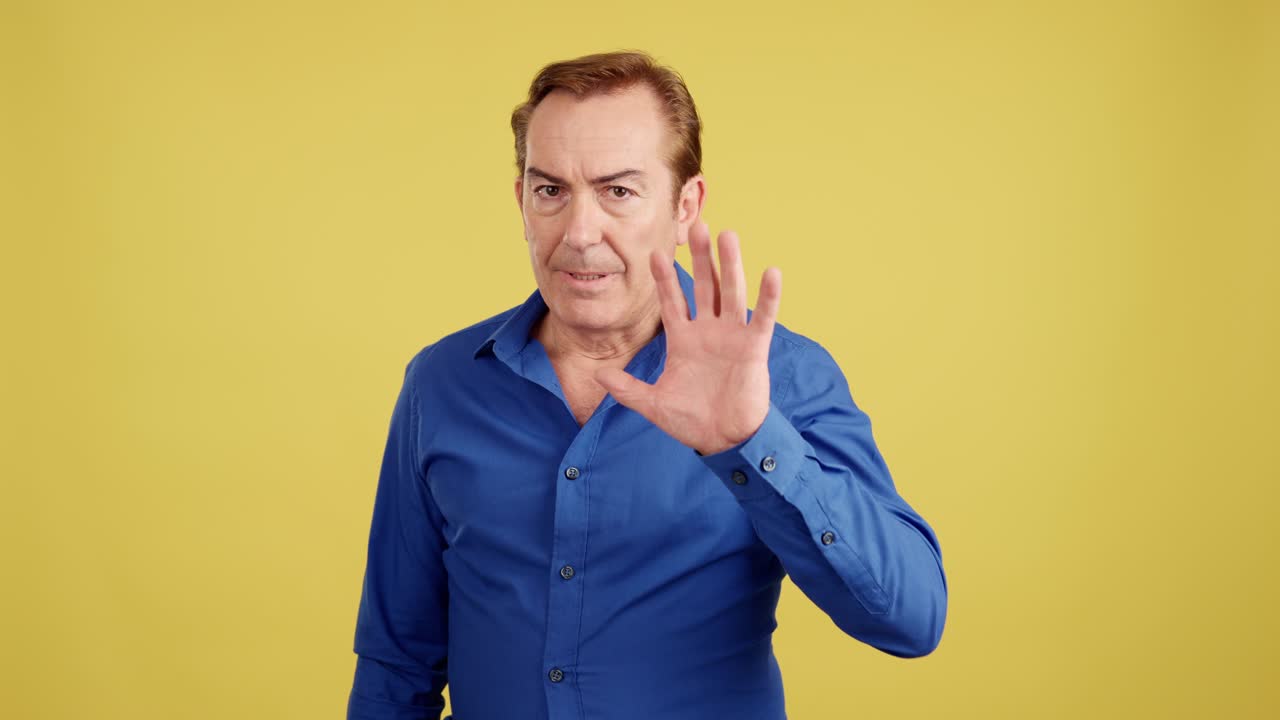 Man showing a stop hand gesture on a yellow background
