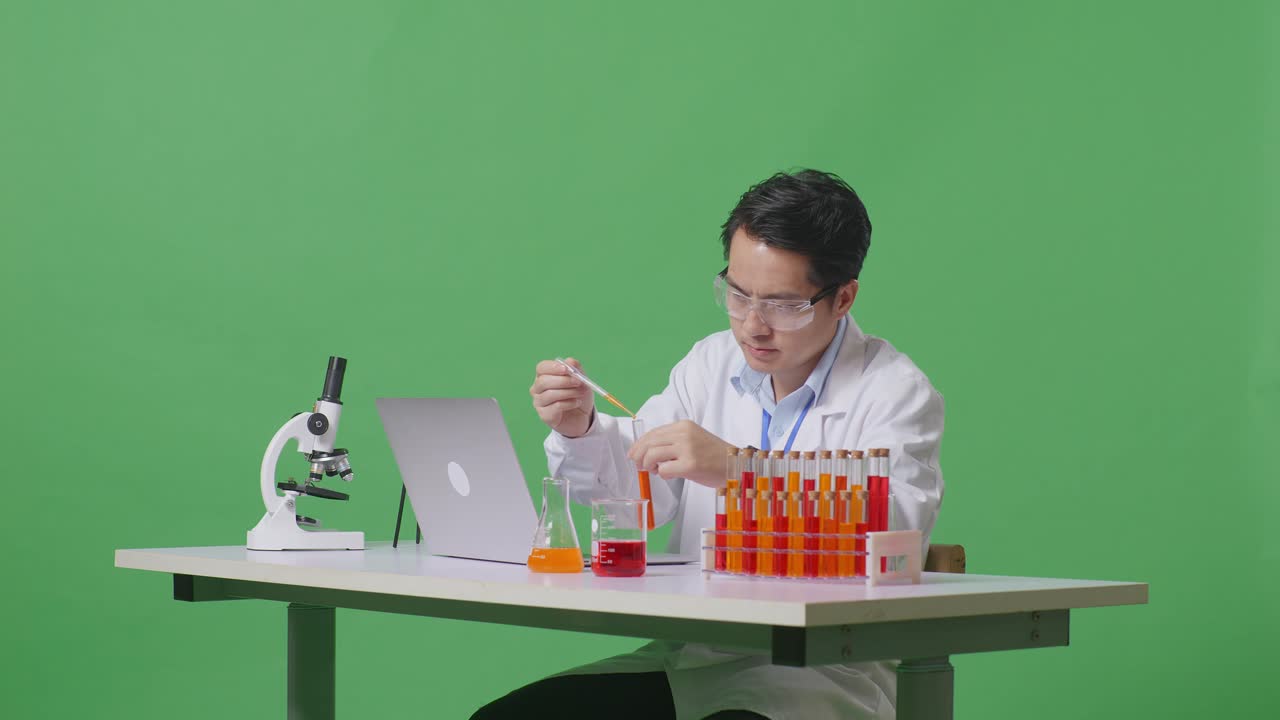 Side View Of Asian Man Scientist Making Experiment With Test Tube And Screaming Goal Celebrating Typing On A Laptop On The Table With Microscope In The Green Screen Background Laboratory