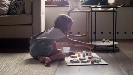 Side-View-Of-A-Blonde-Girl-Sitting-On-The-Floor-And-Painting-Animal-Pieces