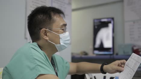 focus on experienced doctor in surgical mask and green uniform checking on patient laboratory test results, side view 4k